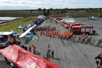 Vista aérea de equipes de combate a incêndios reunidas ao lado de caminhões, equipamentos e tendas em uma área aberta.