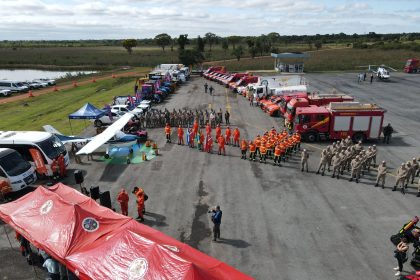 Vista aérea de equipes de combate a incêndios reunidas ao lado de caminhões, equipamentos e tendas em uma área aberta.