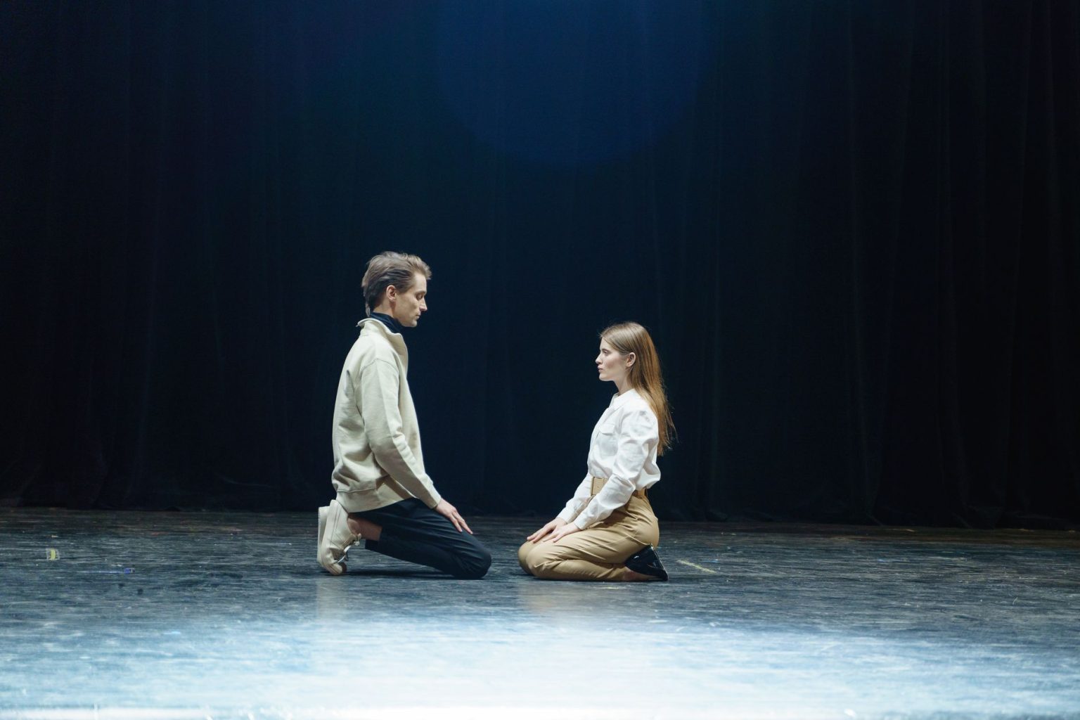 Dois atores participam de uma cena teatral sob um foco de luz no palco.