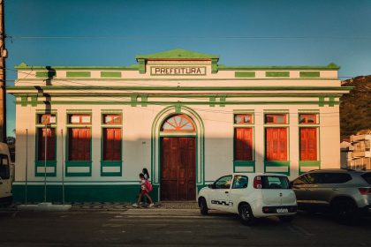Fachada colorida de uma prefeitura brasileira, com pessoas circulando em frente ao prédio ao entardecer