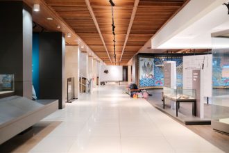 Corredor amplo e iluminado de uma exposição de design moderno, com ambientes e peças expostas.